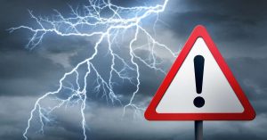 A lightning strike in a dark grey, cloudy sky with a red and white triangle warning sign with an exclamation mark.