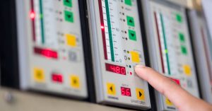A close-up of a frequency converter control panel with green and yellow buttons. A finger presses a grey button.