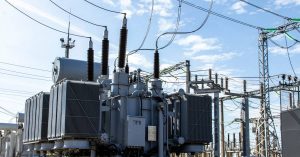 An outdoor site with a high-voltage transformer attached to six different power lines with a cloudy blue sky background.
